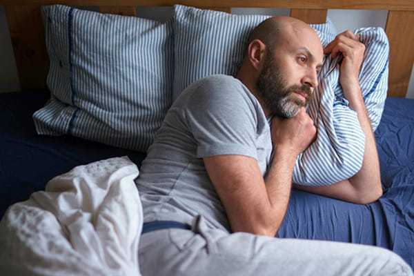 Man sitting on the edge of a bed looking concerned about erectile dysfunction